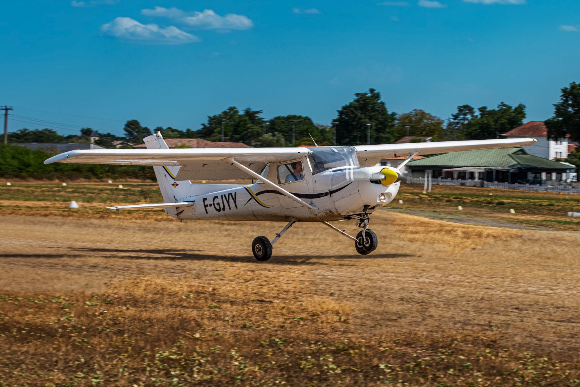 Cessna 152 F-GJYY au ras de la piste en herbe d'Yvrac, club-house en arrière-plan