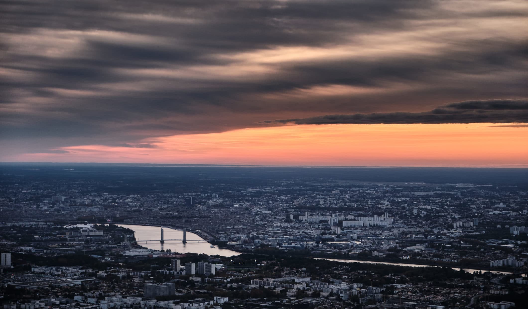 Vue aérienne de Bordeaux et de la Garonne au coucher du soleil, ciel embrasé d'orange, photographiée depuis un avion du club